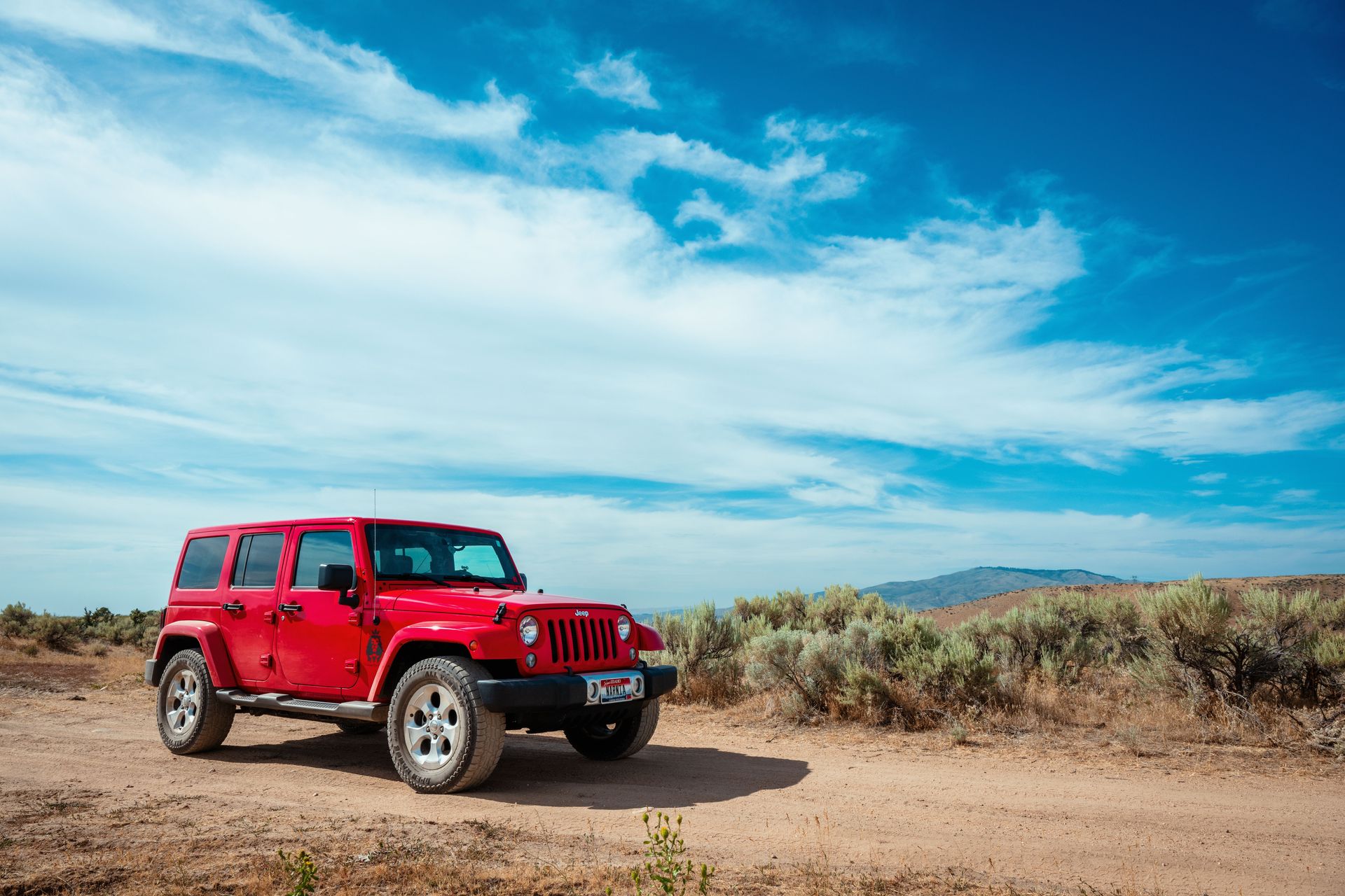 A striking red Jeep Wrangler captured on a rugged dirt road in Boise, Idaho.